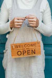 Support small business. Woman holding a handmade sign that says, "Welcome - we are open"